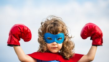 Superhero kid wearing boxing gloves against blue sky background. Girl power and feminism concept