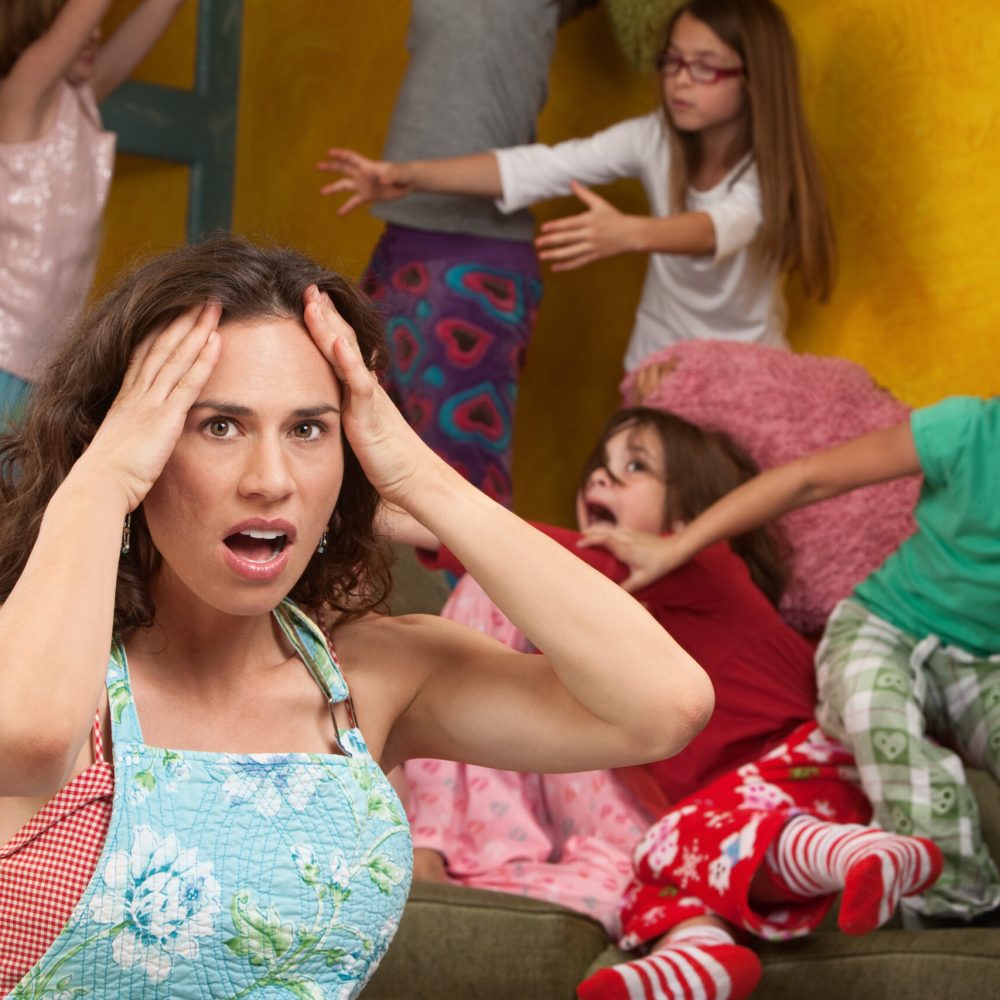 Upset mother with hands on head among mischievous little girls